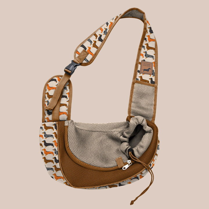 A crossbody sling bag with a brown mesh front pocket, beige and brown sausage dog patterned fabric body, and adjustable strap, shown on a solid beige background.