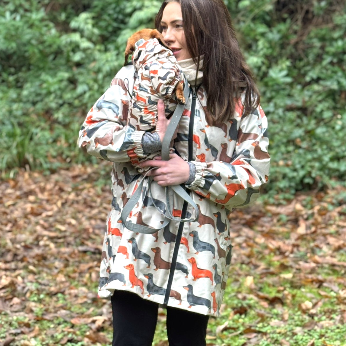 Woman wearing a beige dachshund rain mac with our Sophisticated Sausage print, matching her sausage dog's coat.