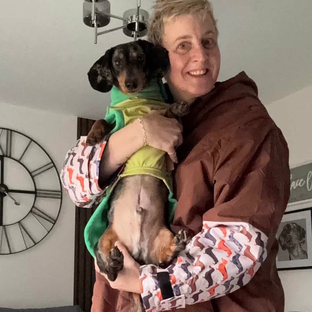 Person wearing the DoxieBurrow waterproof dog walking robe coat while carrying a dachshund.