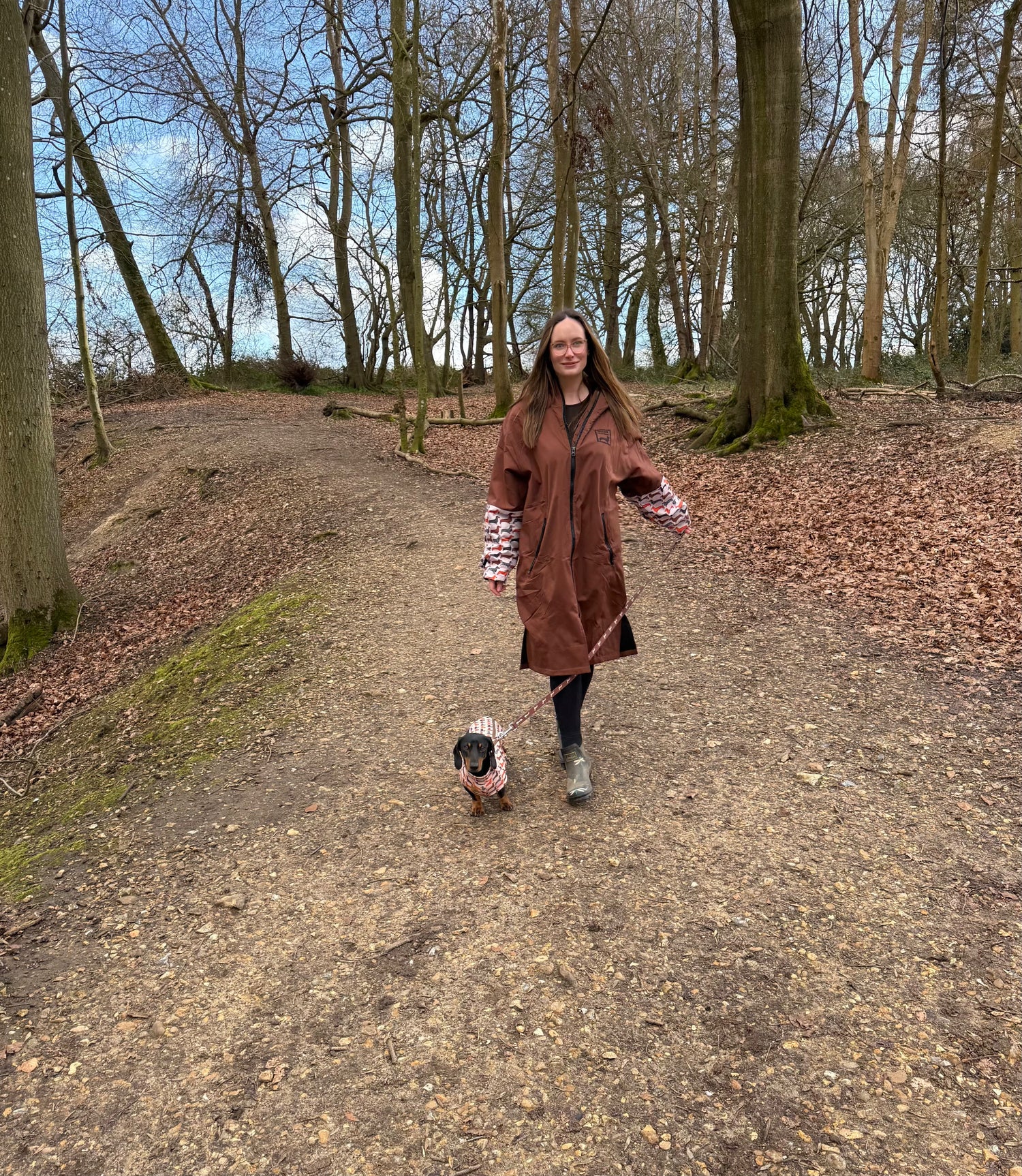 Person wearing the Human Burrow waterproof coat walking a dachshund wearing the Long Dog Zipper harness fleece in the Beige Sophisticated Sausage print with a matching DoxieFlex Biothane lead.
